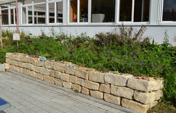 Schulhofmauer der Grundschule Wittlingen mit bemalten Steinen der Schüler Schulhof