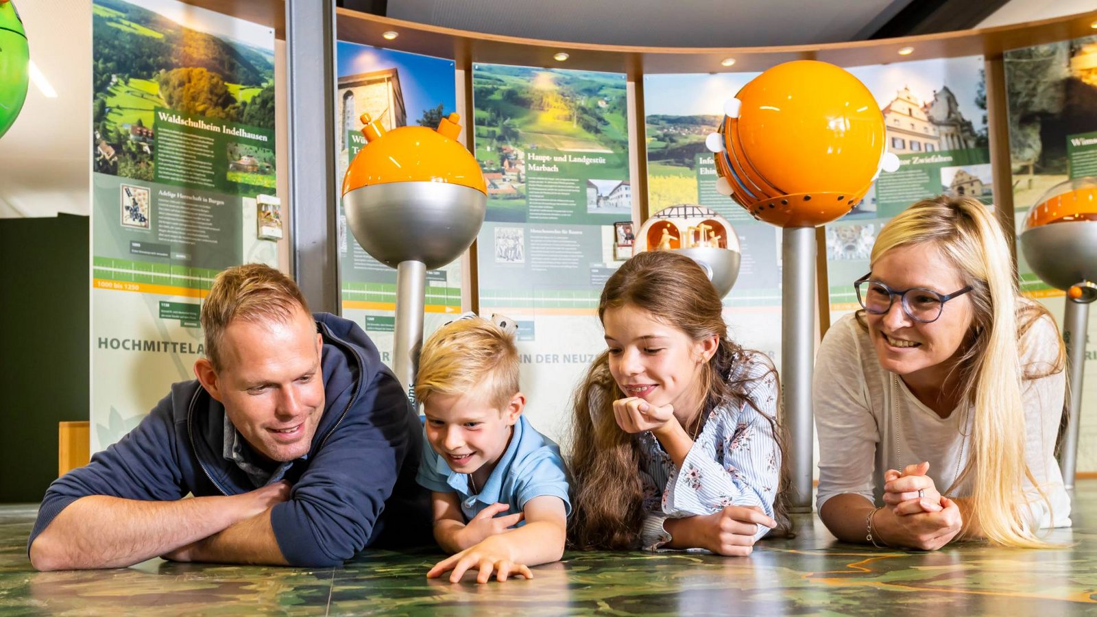 Familie liegt auf dem Boden und beobachtet dort eine Landkarte familie_liegt_auf_dem_Boden